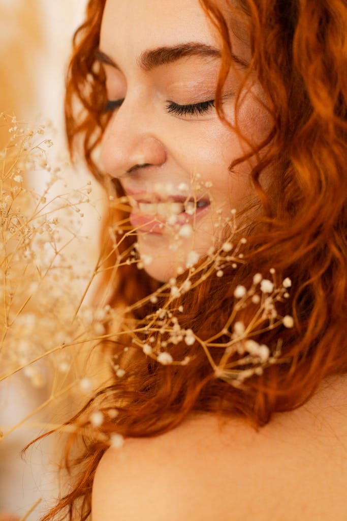 Close-up portrait of red-haired woman with delicate flowers, serene expression.